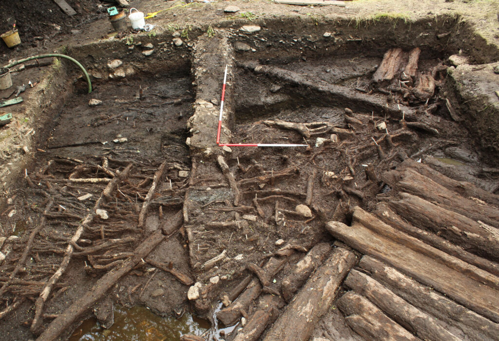Mid-excavation of roundhouse ST3 with the trackway logs in the front and the threshold beams in the back Mid-excavation of roundhouse ST3 with the trackway logs in the front and the threshold beams in the back.