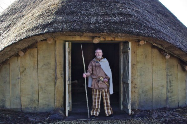 The reconstructed roundhouse with a reenactor wearing possible Iron Age costume